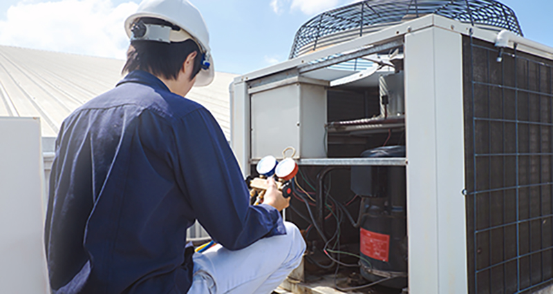Photo of a male HVAC technician servicing a rooftop air conditioner unit