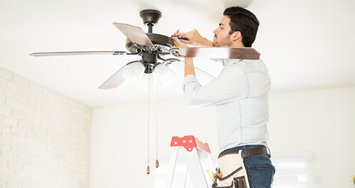 Man on a step ladder installing a ceiling fan