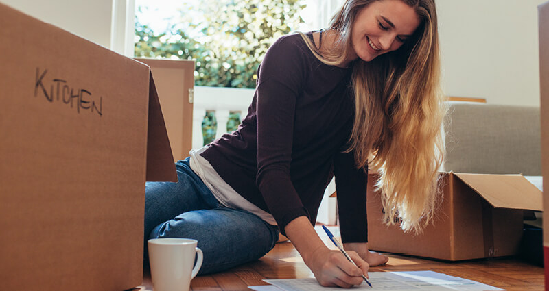 Smiling woman sitting with moving boxes on the floor making a list