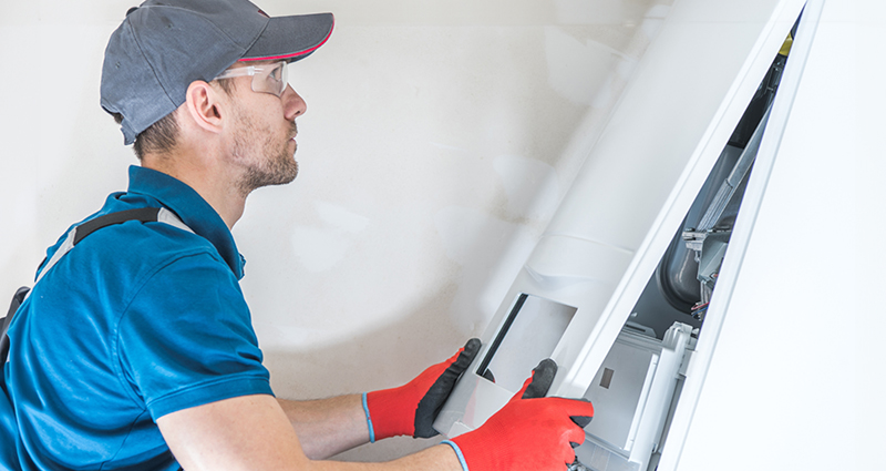 A male maintenance professional in a blue shirt fixing a furnace