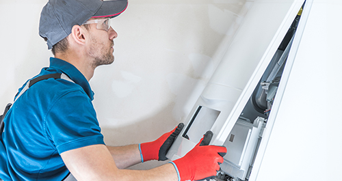 A male maintenance professional in a blue shirt fixing a furnace