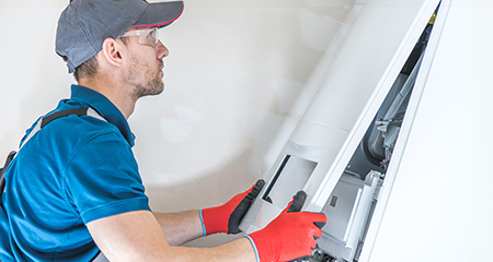 A male maintenance professional in a blue shirt fixing a furnace