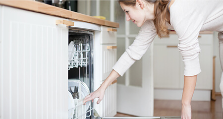Young woman putting dishes in the dishwasher