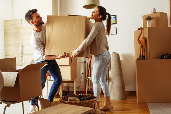 young-couple-moving-helping-one-another-carry-big-box-medPromo